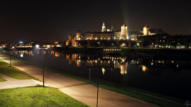 Zdjęcie zrobione z Mostu Grunwaldzkiego, licząc od pierwszego planu, znajdują się Bulwar Poleski, rzeka Wisła i wzgórze Wawel wraz z Zamkiem Królewskim i bazyliką archikatedralna św. Stanisława i św. Wacława.
